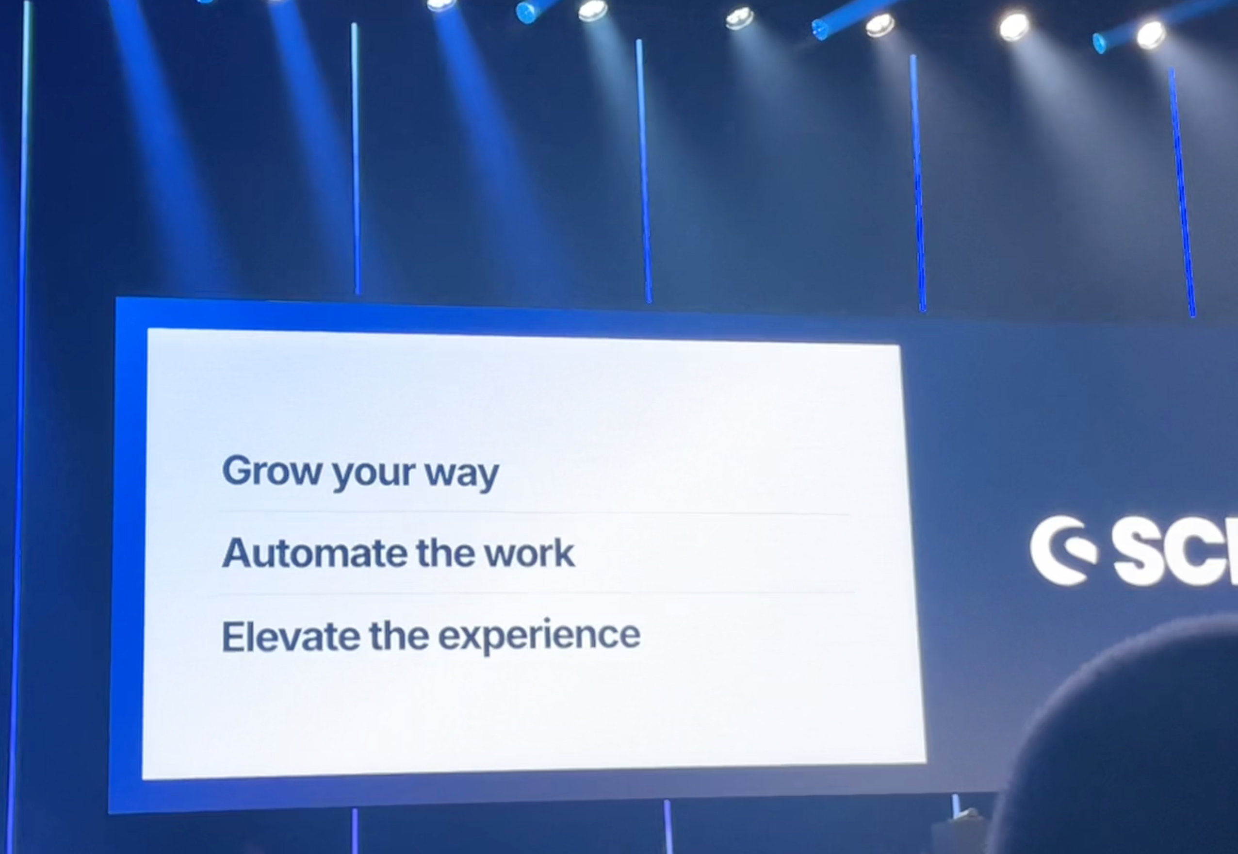 Bühnen-Screen auf dem Shopware Community Day mit dem Claim „Grow your way · Automate the work · Elevate the experience“